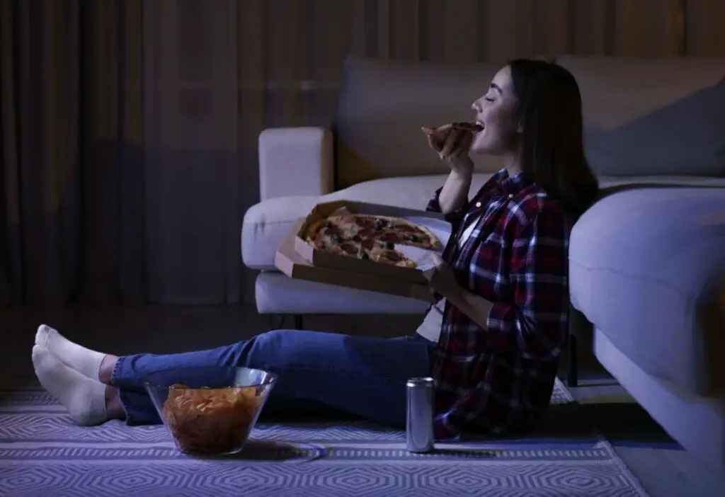 A girl eating a pizza and chips while watching a TV